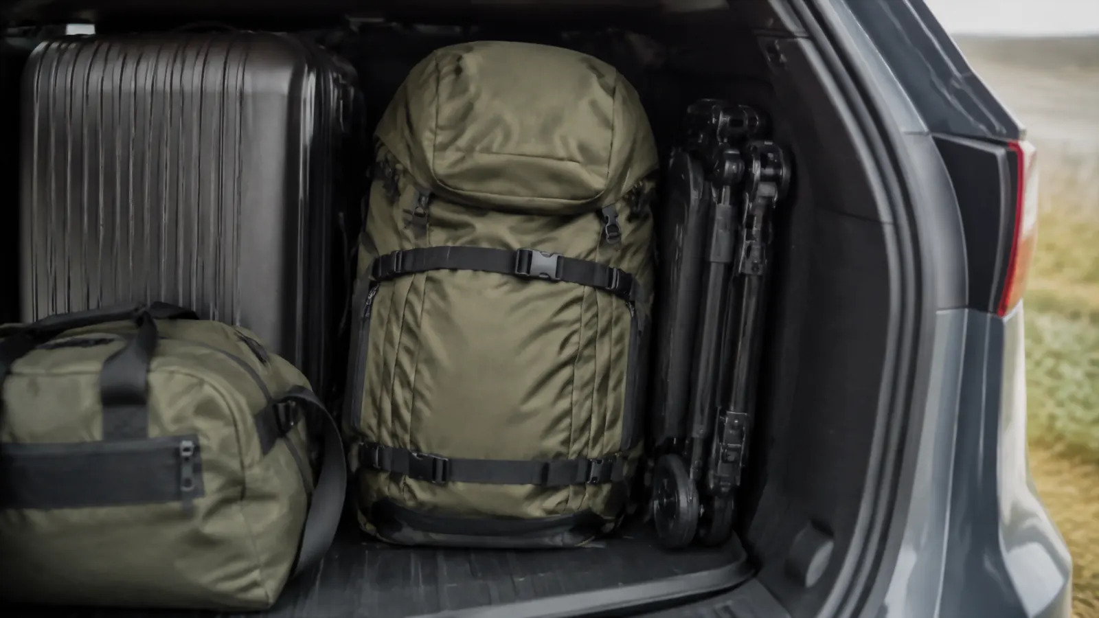 Folding luggage cart collapsed flat and tucked into the trunk of a car next to other bags