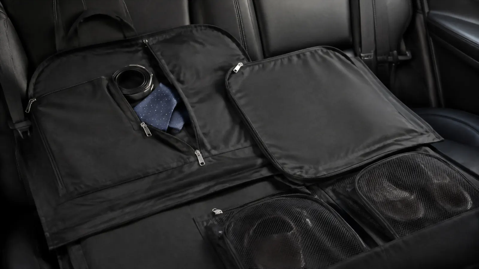 Garment bag laid across the back seat of a car with the accessories pocket unzipped, belt and tie tucked inside