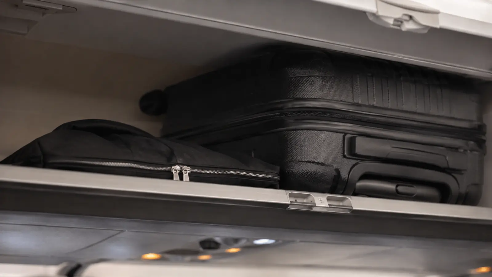 Folded garment bag wedged under a rollaboard suitcase in a cramped regional jet overhead bin