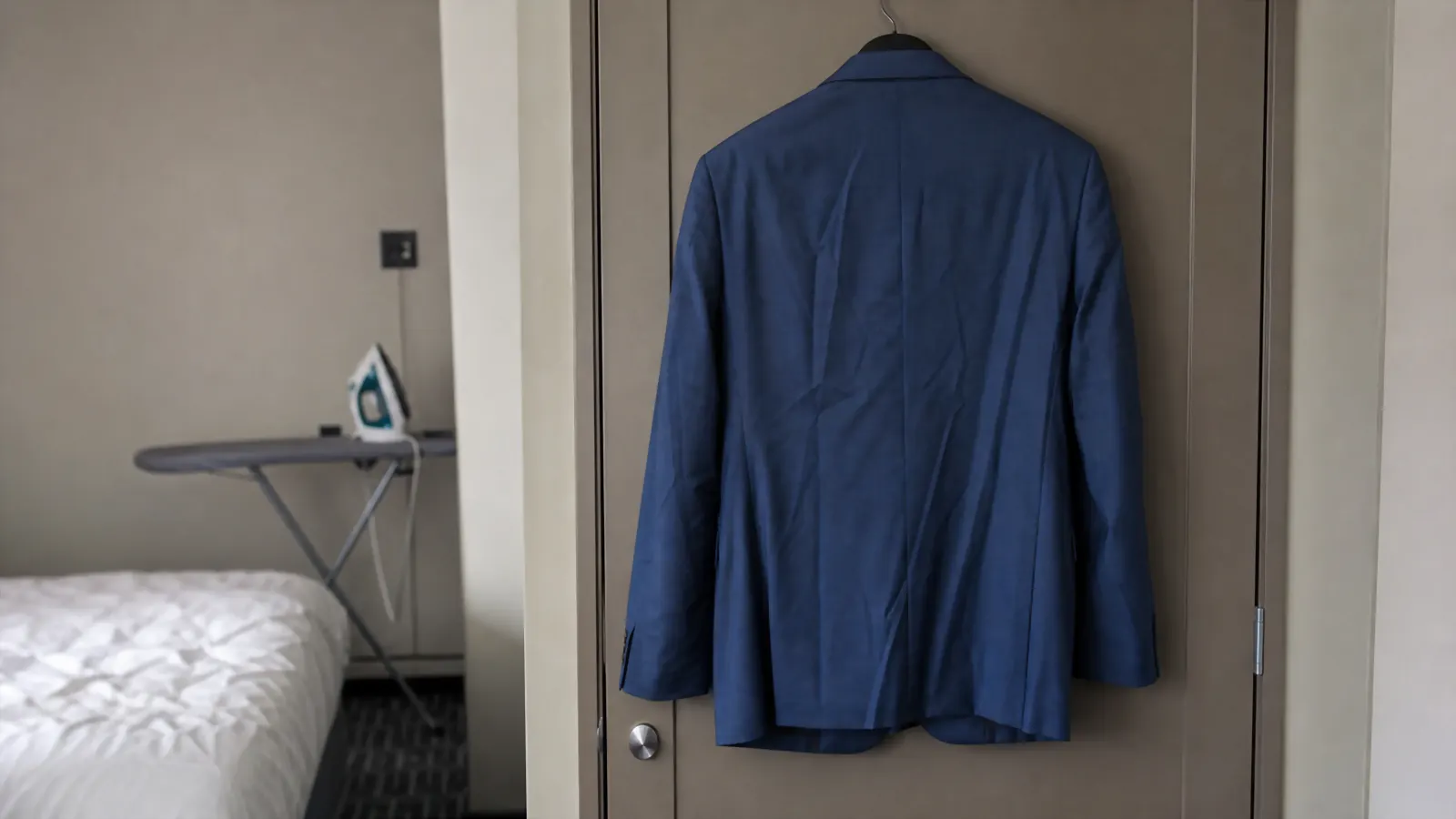 A slightly creased suit jacket hanging on a hotel closet door, needing a full press before a meeting