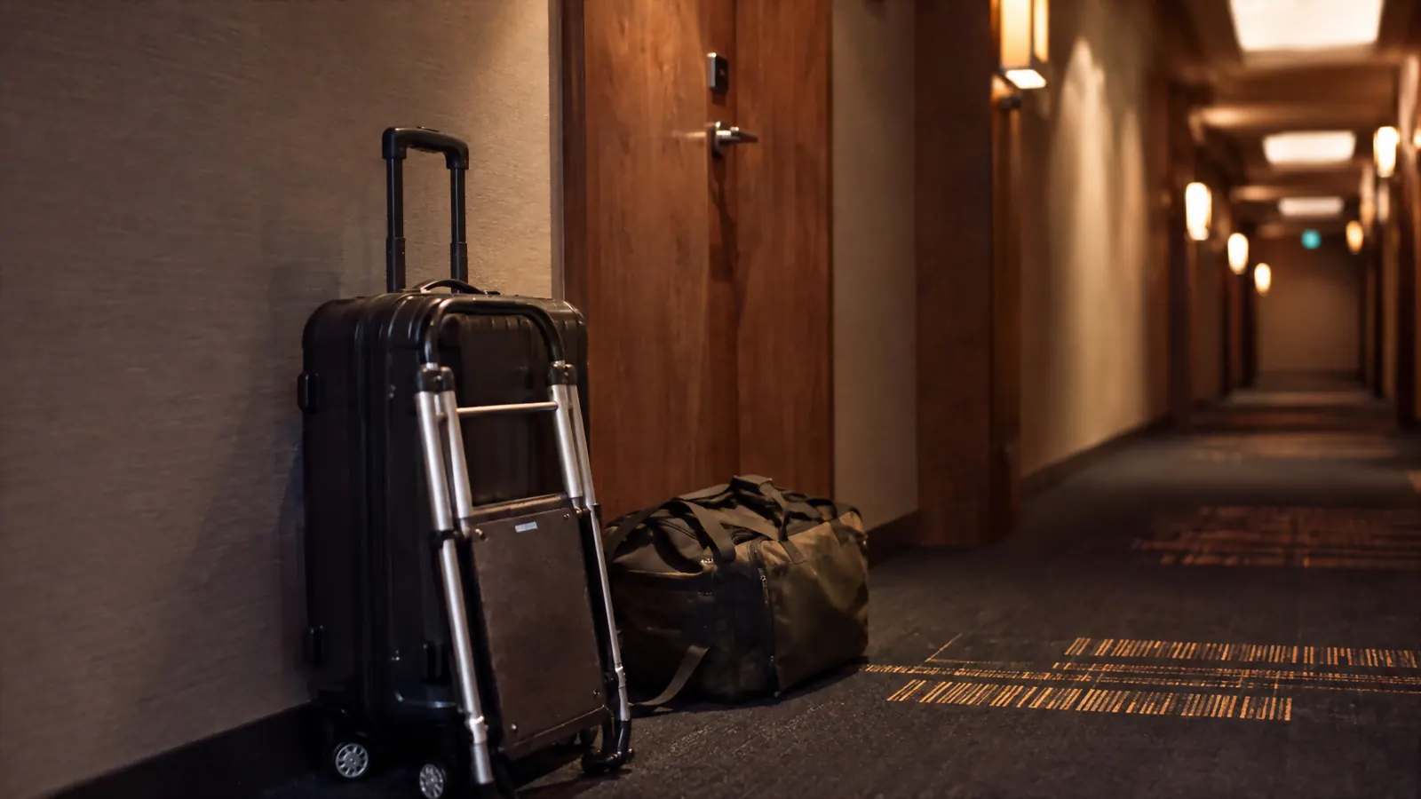 A folded hand truck leaning against the wall of a hotel hallway beside luggage outside a room door