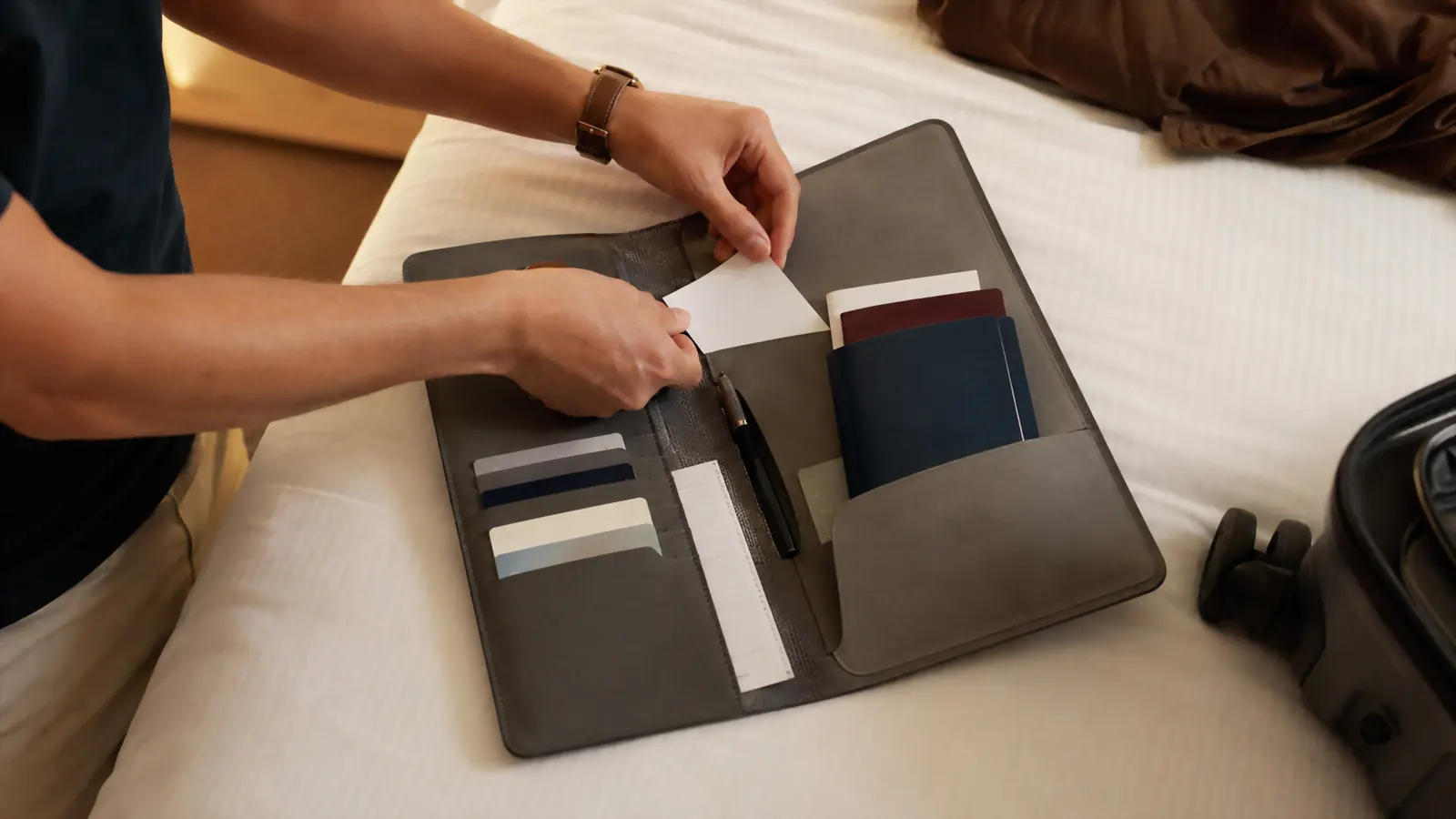 Flatlay of a family's travel documents, insurance cards, and boarding passes being packed into a gray organizer on a hotel bed